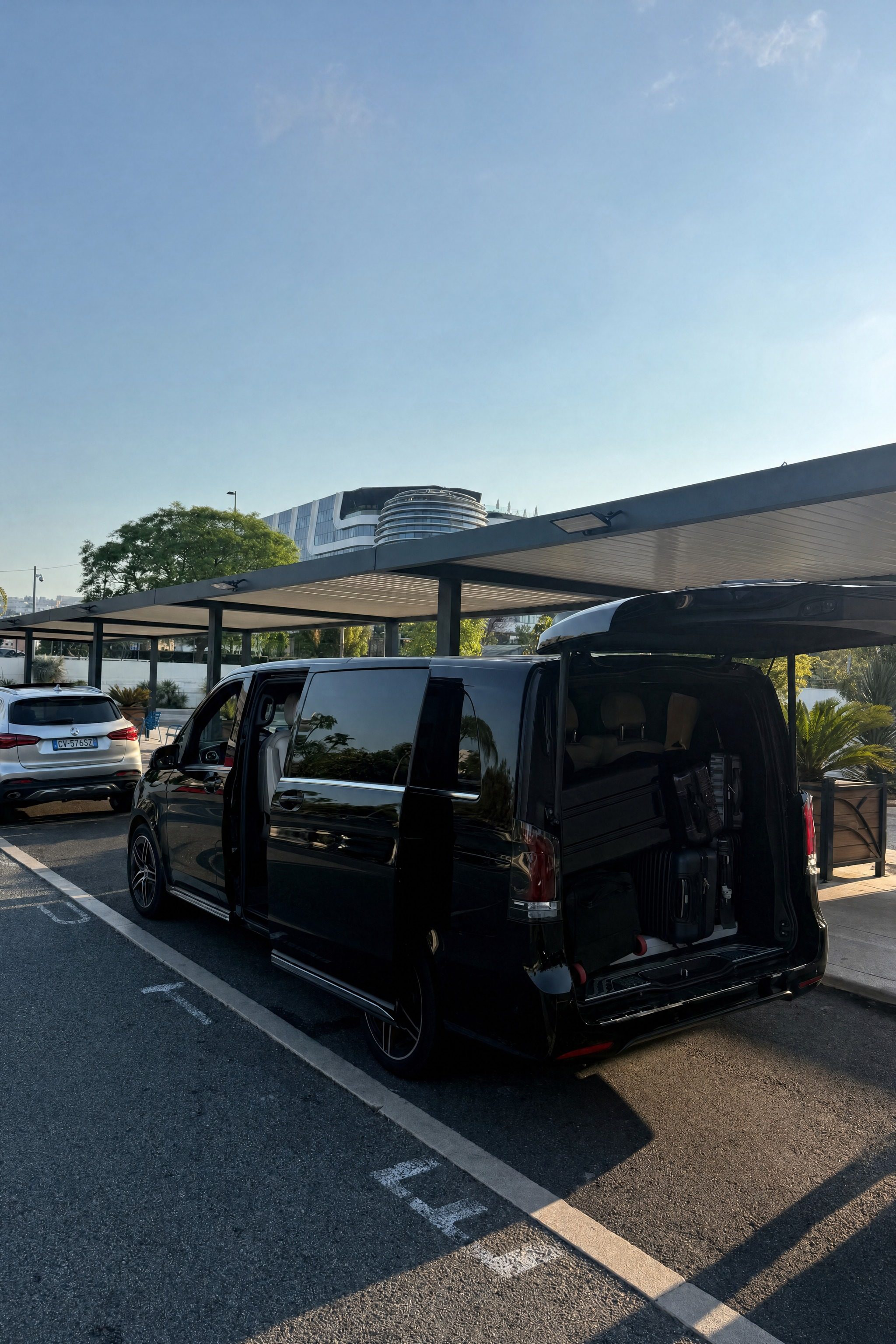 Le van à l'arrêt, coffre ouvert, bagages chargés sous l'auvent d'un établissement